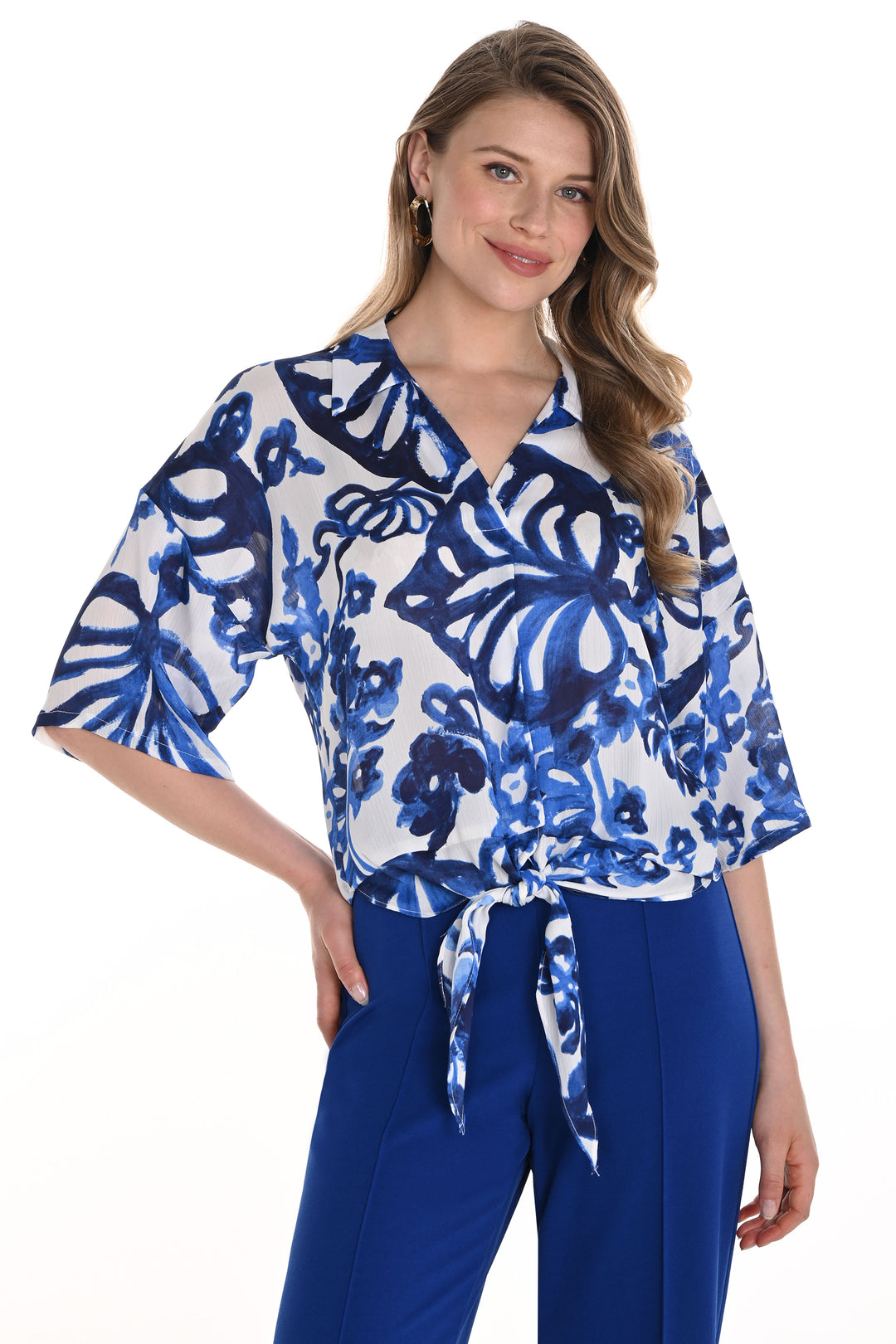 Frank Lyman Spring 2025 This vibrant print features a bold floral design and a tie knot at the front hem for a touch of style. Made with a comfortable woven material, the short and wide sleeves add an effortlessly chic touch.