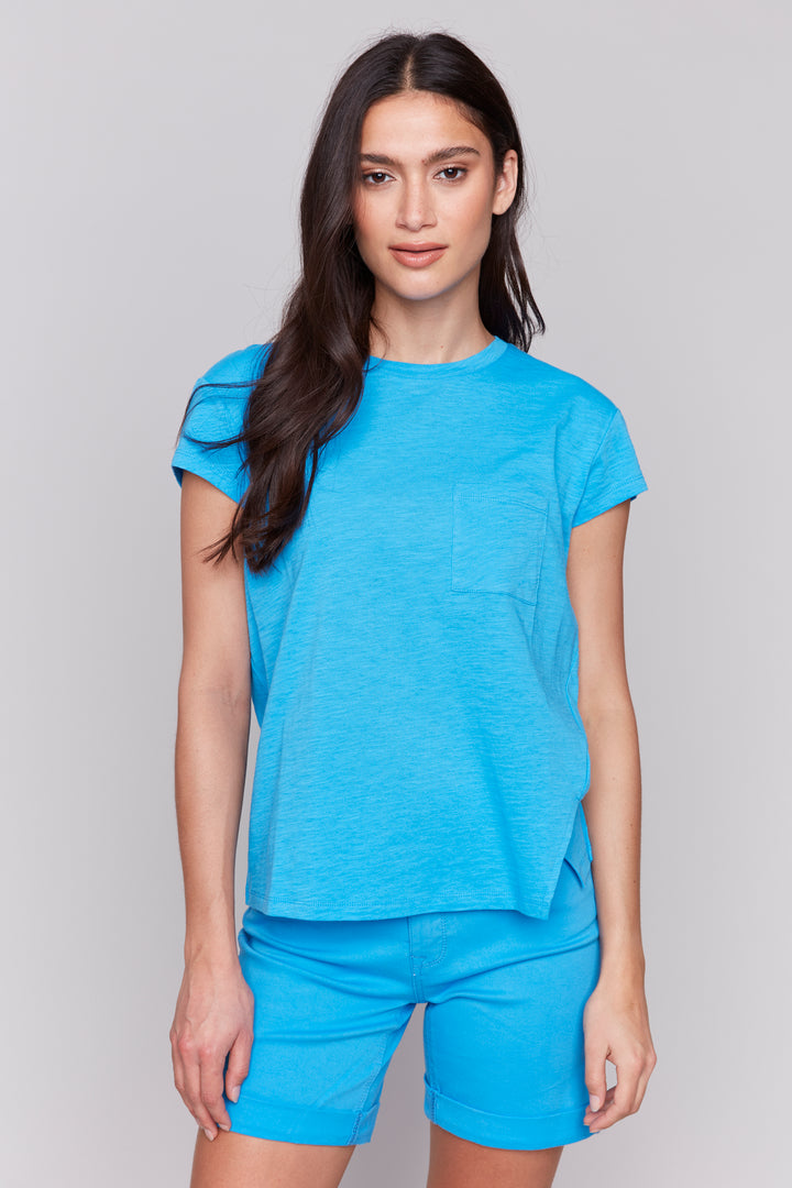 Charlie B Spring 2025 Made from all organic cotton, this classic tee features a front slit cut detail and a chest pocket. With double stitch hem and short cap sleeves, it's a timeless piece with a modern twist.