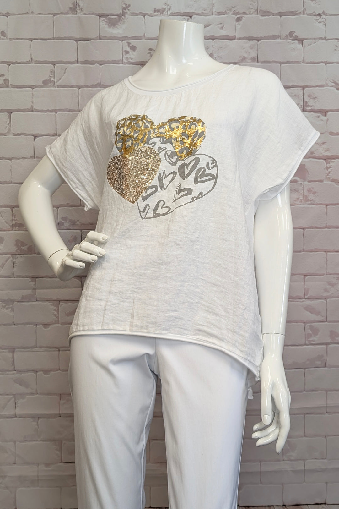 ANGELA MARA Spring 2025 This White Triple Heart Top combines a light linen and cotton blend for breathable comfort, ideal for warm days. Featuring three heart motifs accented with gold and glitter, it adds a subtle touch of sparkle to your outfit. 