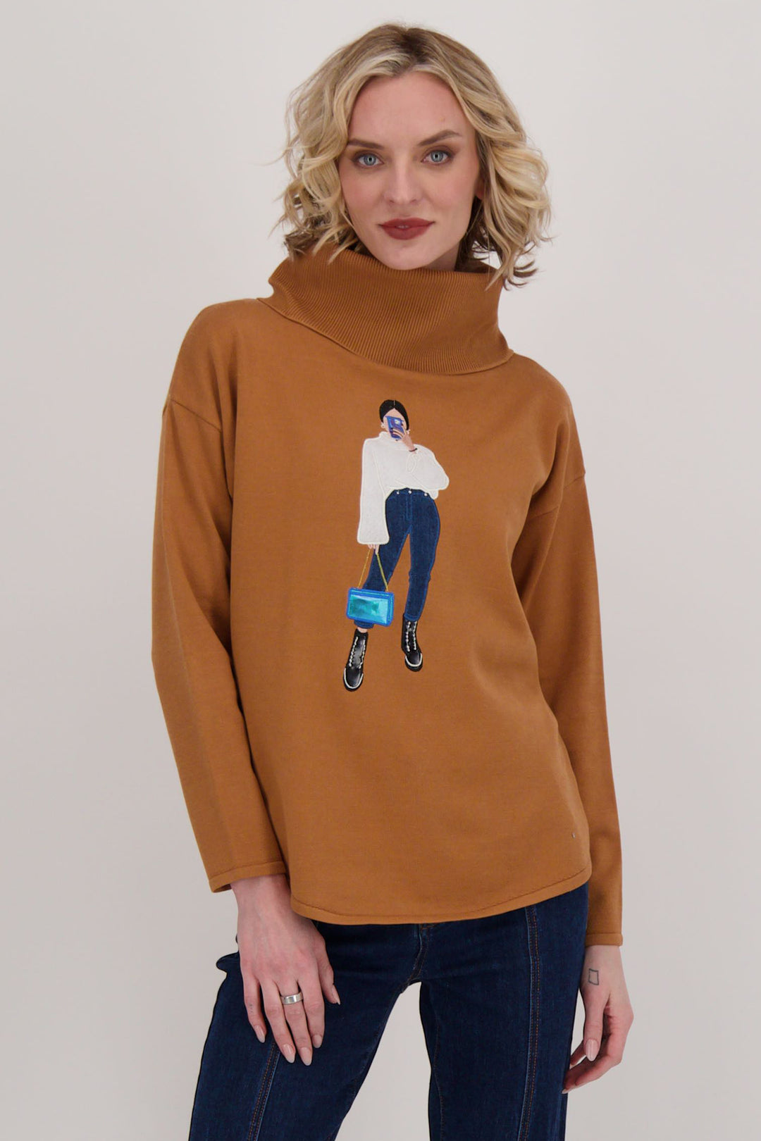 Gabby Isabella Fall 2024 The playful girl on the phone design adds a touch of whimsy to this bold camel-colored sweater. Plus, the tie lacing detail at the back and relaxed fit make it the perfect addition to your wardrobe.