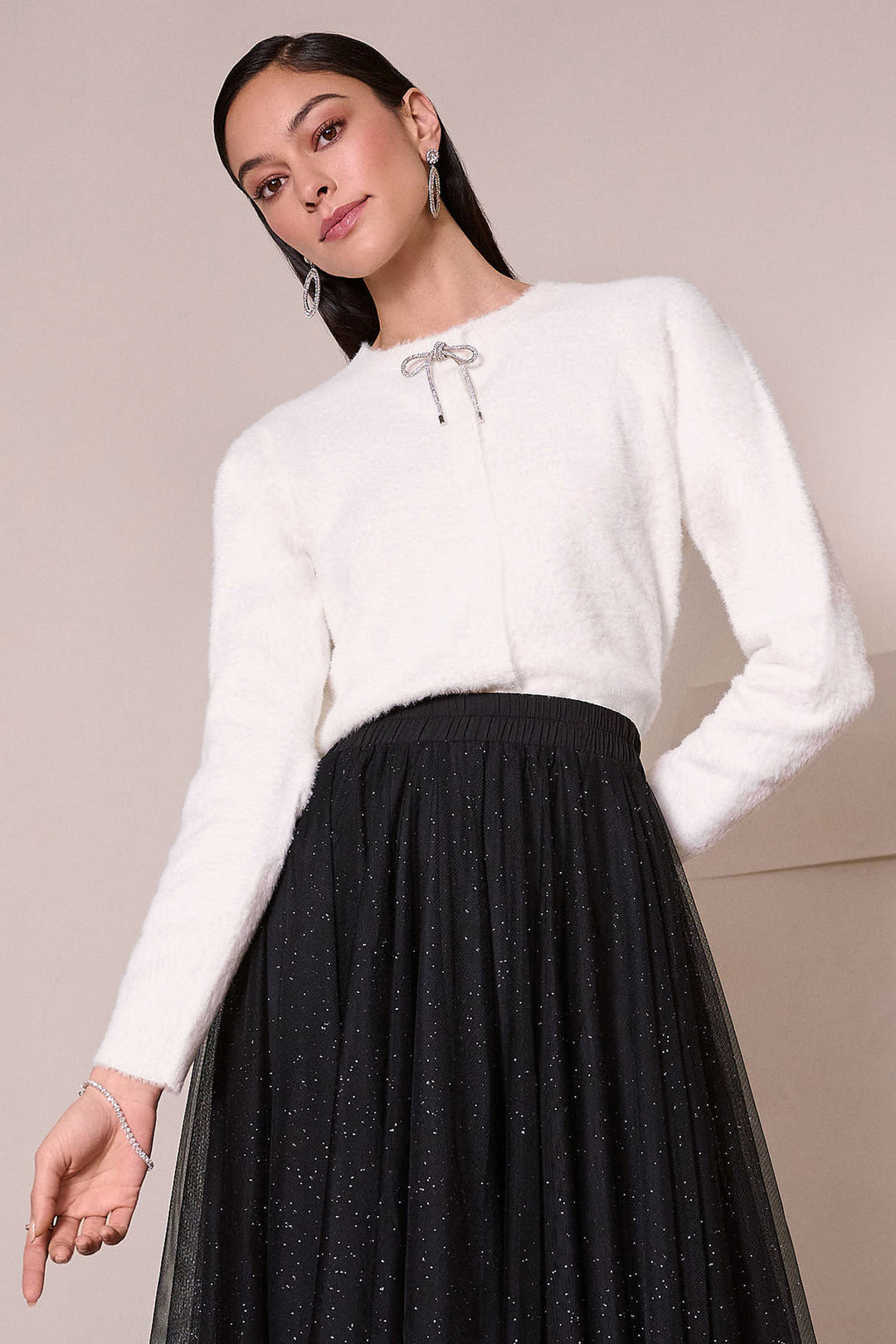 Joseph Ribkoff Fall 2025 
 Crafted from soft feather yarn fuzzy knit fabric, it is accented by a delicate rhinestone bow tie, adding a refined touch. 