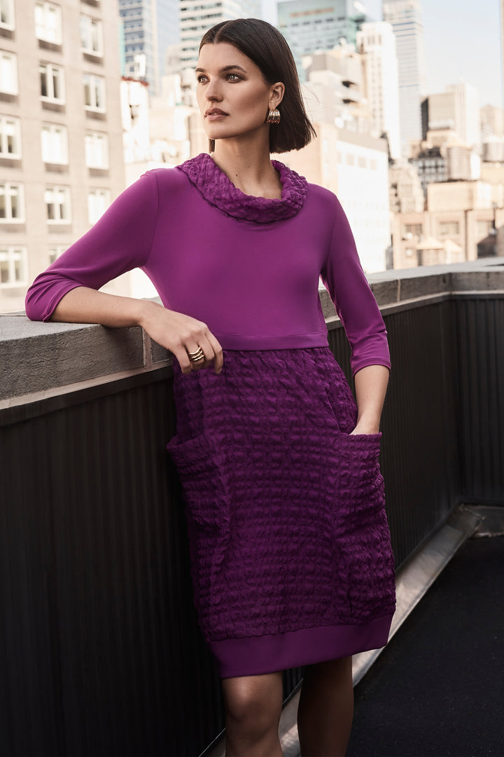 Joseph Ribkoff Fall 2024 Featuring a contrast cowl neck, 3/4 length sleeves, and a soft, light fabric, this dress is both comfortable and stylish. The contrast bubble texture skirt in the lower half adds a unique touch and even has pockets for convenience.